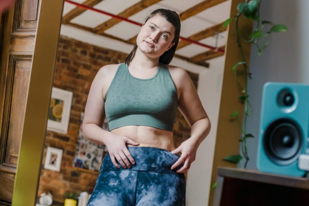 Woman confidently poses in activewear, embracing body positivity in a cozy indoor setting.