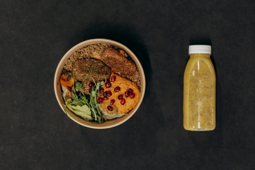 A vibrant vegan bowl with quinoa, fresh vegetables, and a smoothie bottle against a dark backdrop.