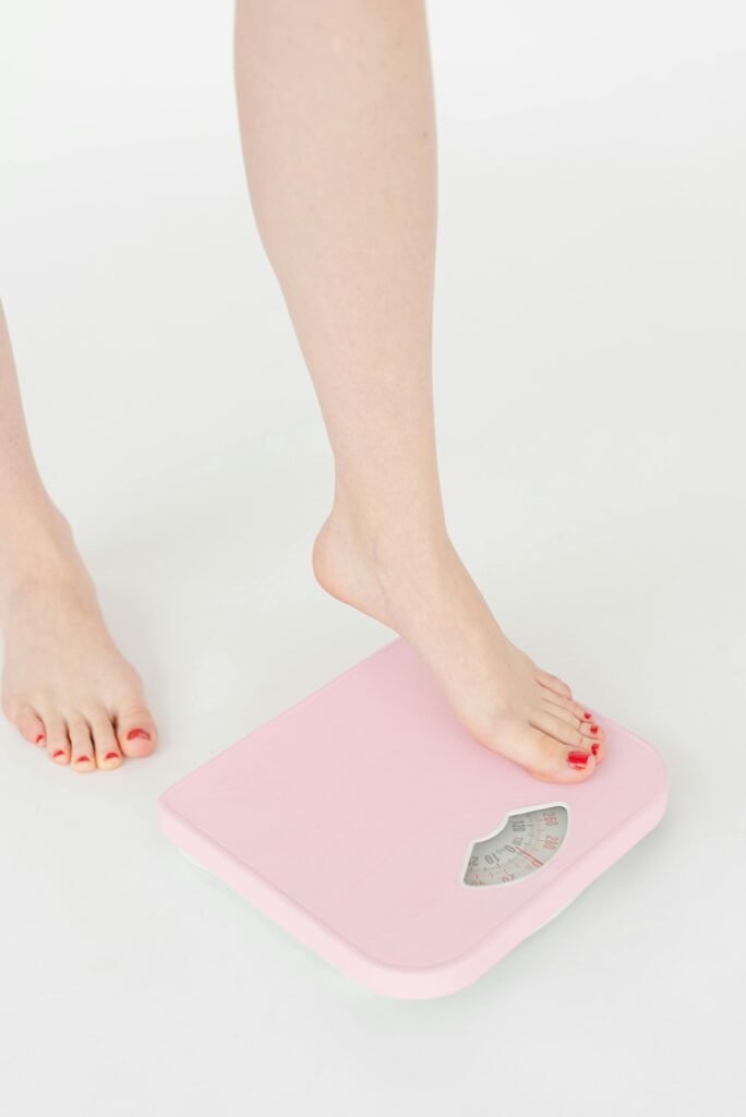 A woman's feet with red nails stepping onto a pink weight scale, symbolizing health and wellness.